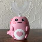 Na obrazku widać jak szczoteczka elektryczna w kolorze różowym jest postawiona na biurku.